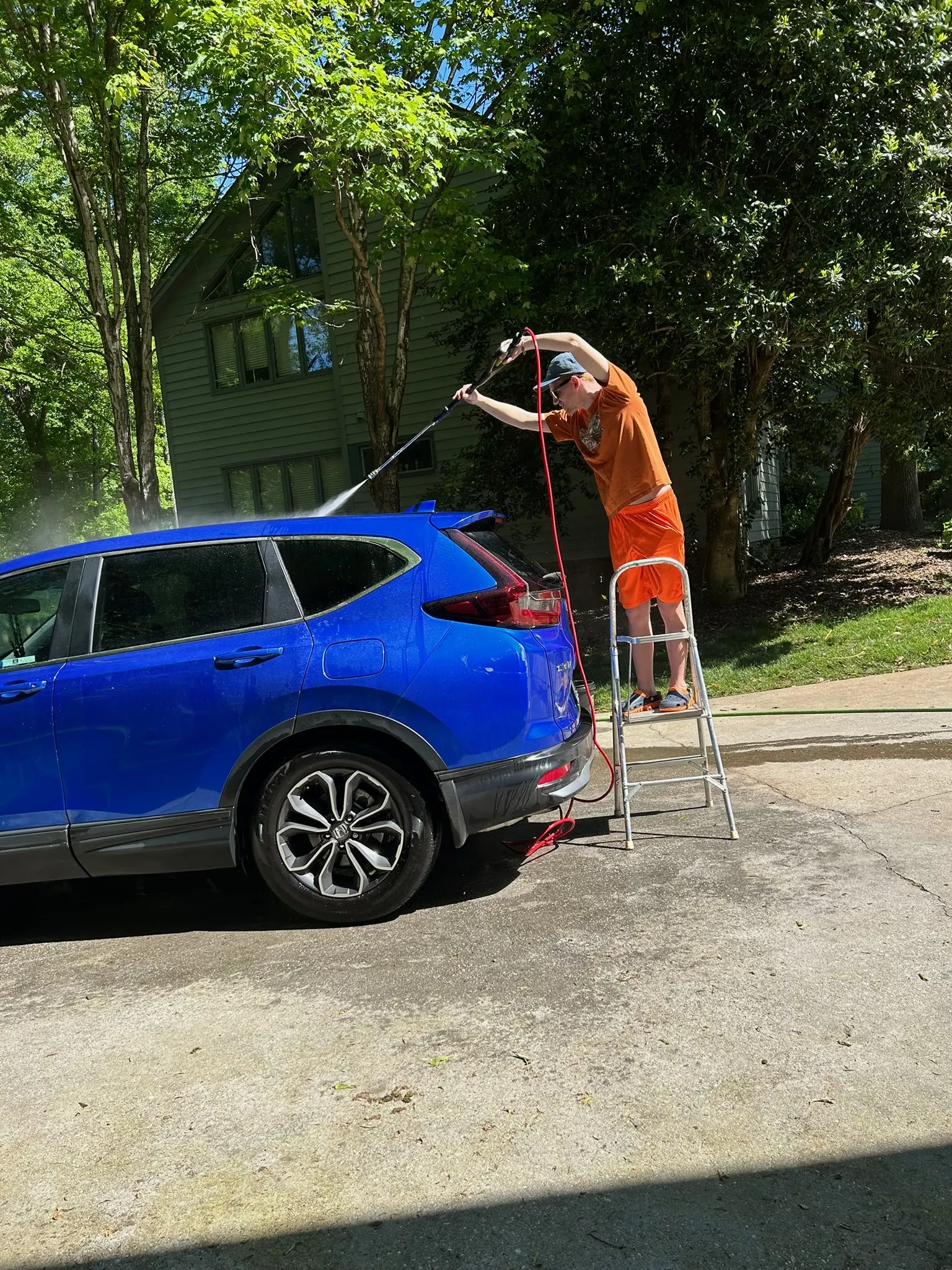 Alexander rinsing a blue SUV during detailing